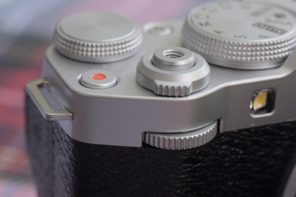 A view of the front command dial of the Fuijfilm X-M5. Above is the shutter button, the record button with a red dot, the reat dial and the mode dial. Below the silver top part of the camera is the black grip.