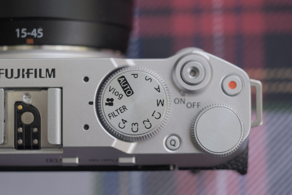 The top plate of the X-M5. From left to right: the hot shoot, the mode dial, the Q button on the bottom side, the shutter button with on/off switch on the top edge, the back control wheel on the bottom edge and the red dotted record button just above the wheel.
