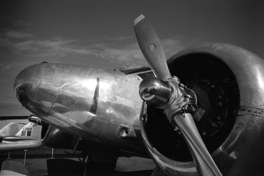 A black & white picture of the WW2 era aircraft up close. To the right the propeller. To the left further away the shiny nose of the Beechcraft Expedition with the propeller reflecting in it.