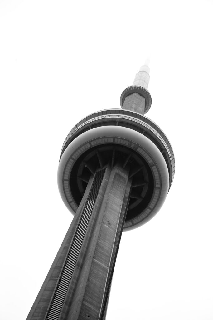 A black & white image.
A structure pointing up towards the top left. A donut shape interrupt the flow of the structure and the tip is partially blurred by the fog. It is the CN Tower.